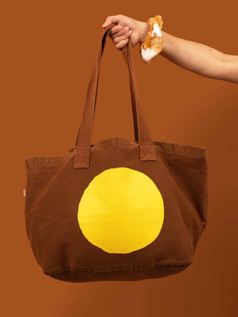 Large brown canvas tote with a bright yellow circle screen printed on it. 