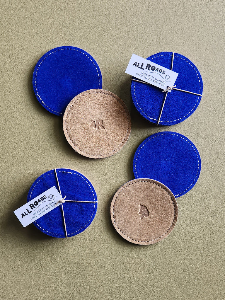 Set of 4 suede coasters, 1 side bright cobalt and the other side tan with AR brand. 