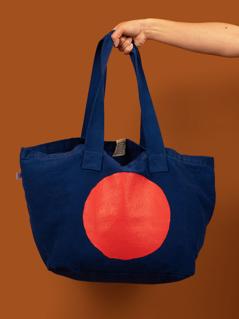 Large cobalt blue canvas tote bag with a bright red circle screen printed on it. 