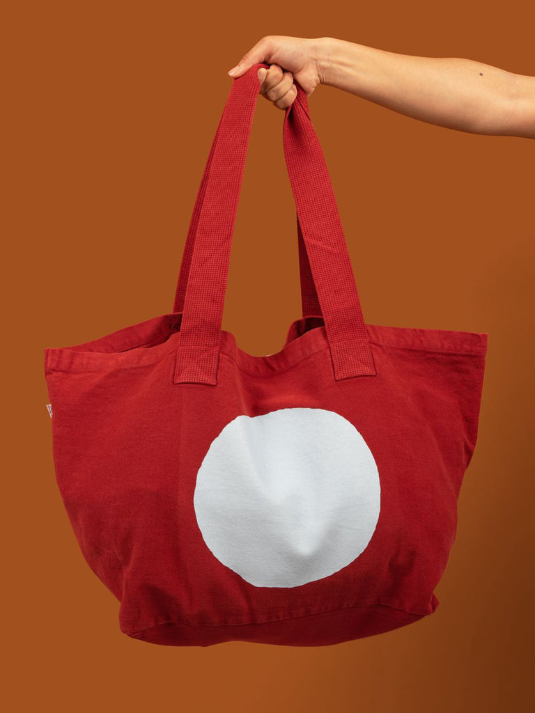 Large red tote bag with a pale blue circle screen printed on it.
