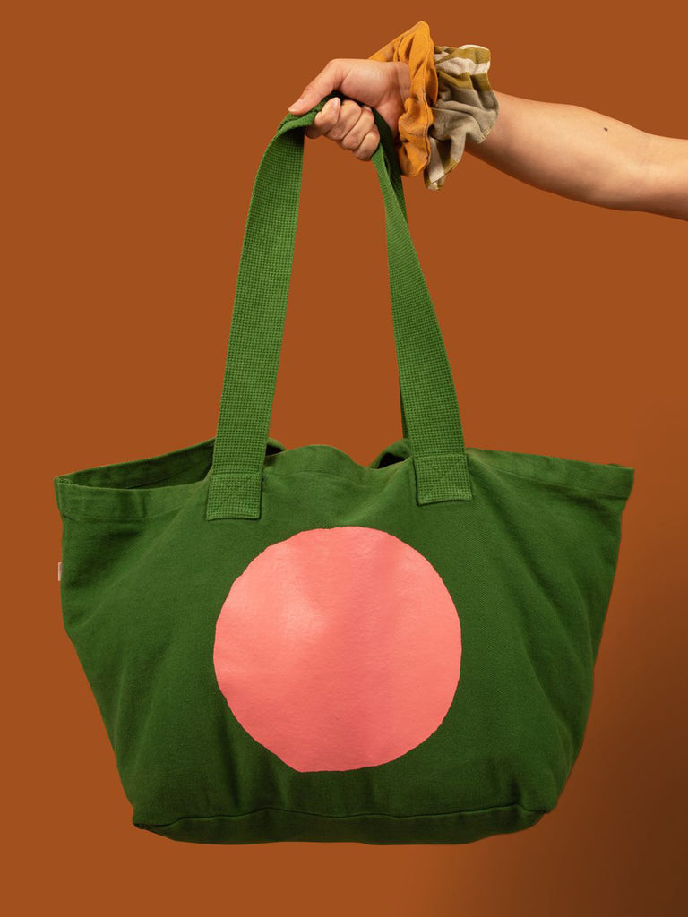Large kelly green canvas tote bag with a pink circle screen printed on it. 