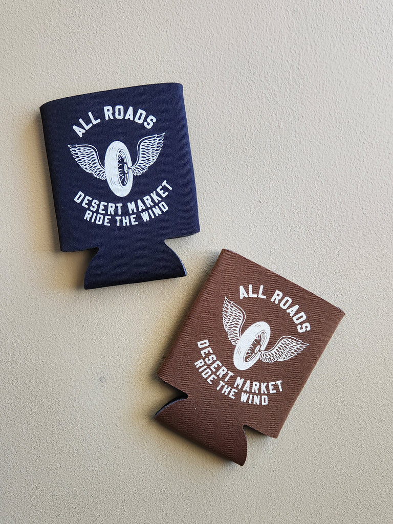 black and brown drink insulator holders with the text All Roads Desert Market Ride The Wind and a wing and wheel logo.