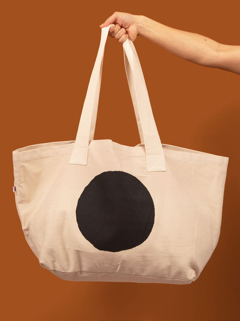 Large natural canvas tote bag with a black circle screen printed on it. 